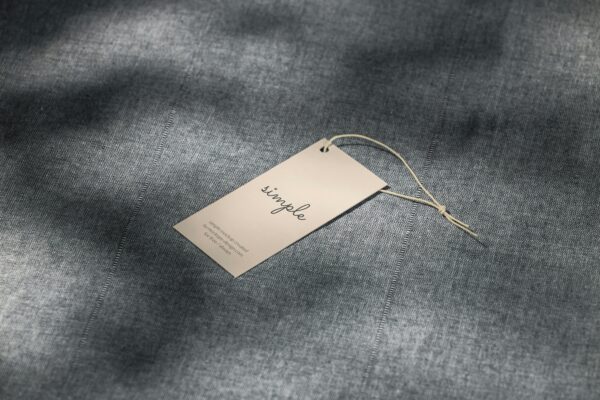 A simple clothing tag resting on a textured gray fabric surface with soft lighting.