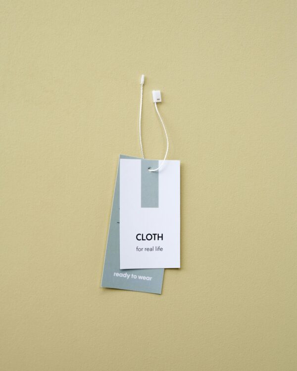 Close-up of minimalist clothing labels against a beige backdrop, featuring 'CLOTH for real life'.