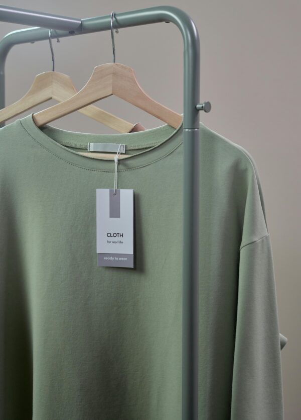 Close-up of a green shirt on a hanger with label tag on a minimalist clothing rack.